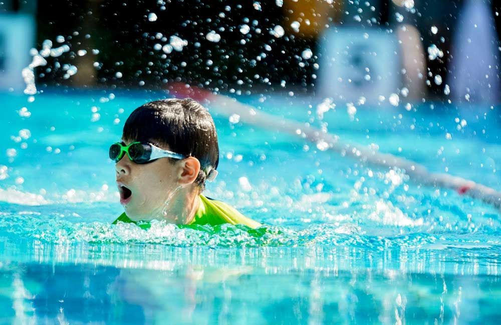 A young boy wearing goggles is swimming in a pool.
