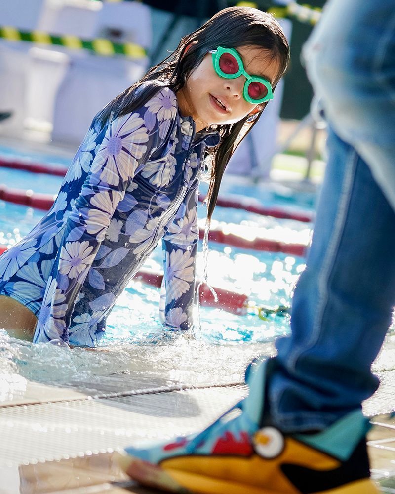 A little girl wearing sunglasses is crawling out of a swimming pool.
