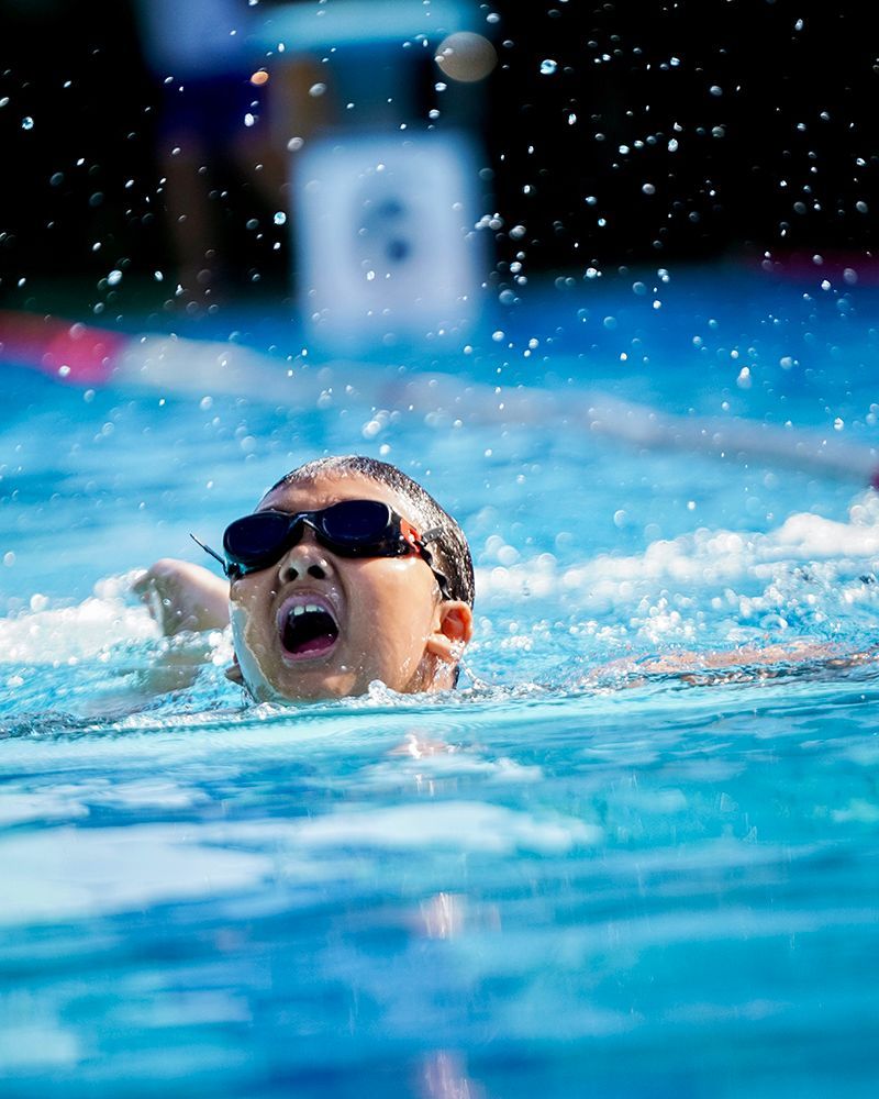 A young boy wearing goggles is swimming in a pool.