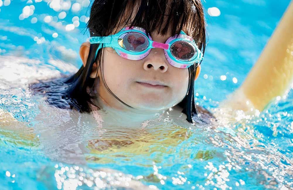 A young girl wearing goggles is swimming in a pool.
