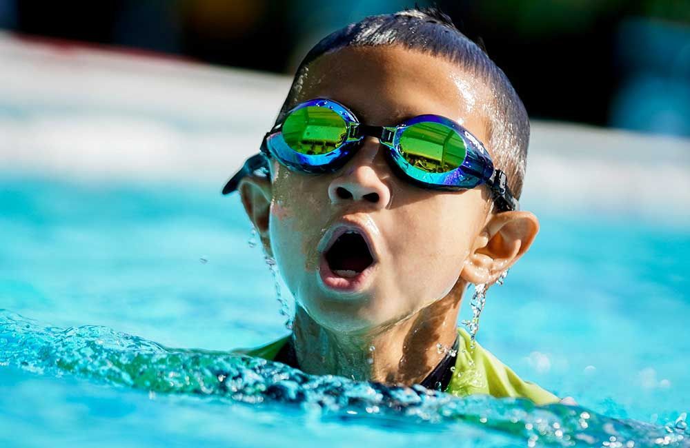 A young boy wearing goggles is swimming in a pool.