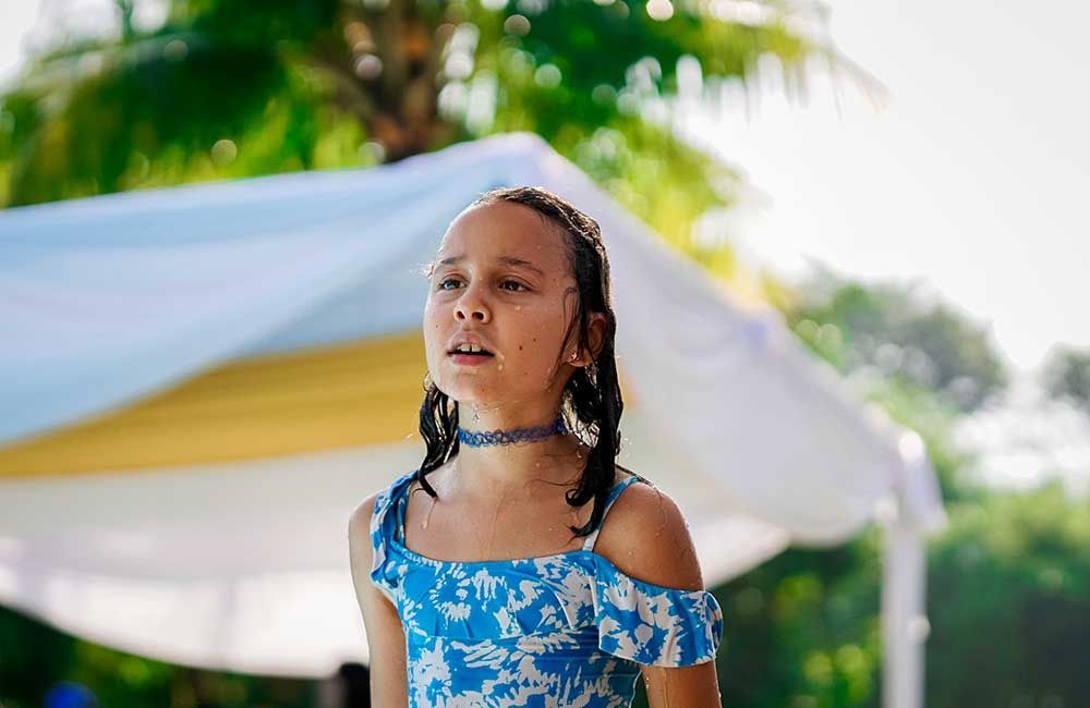 A young girl in a blue dress is standing in front of a white tent.