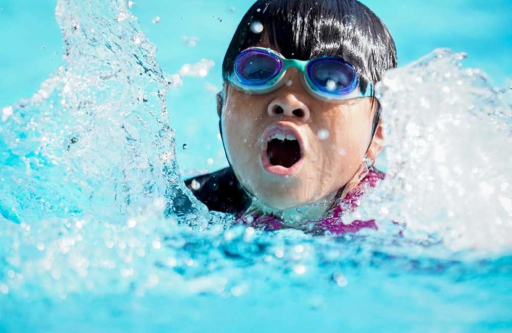 A young girl wearing goggles is swimming in a pool.