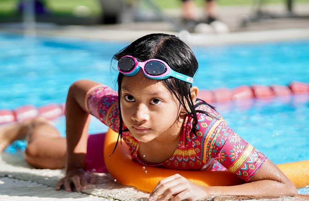 A little girl is laying on the edge of a swimming pool.