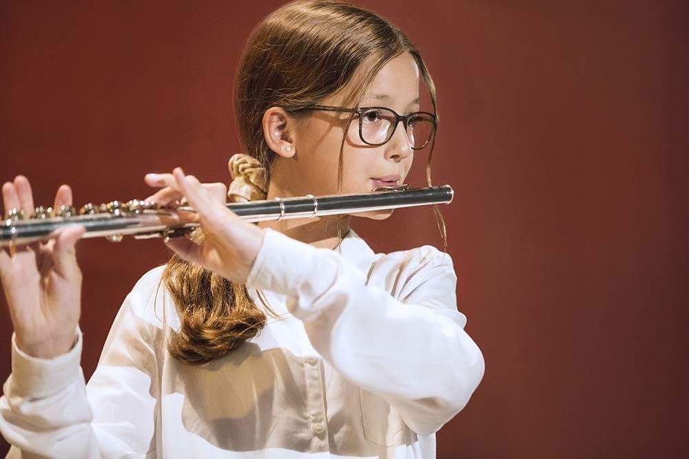 A young girl wearing glasses is playing a flute.