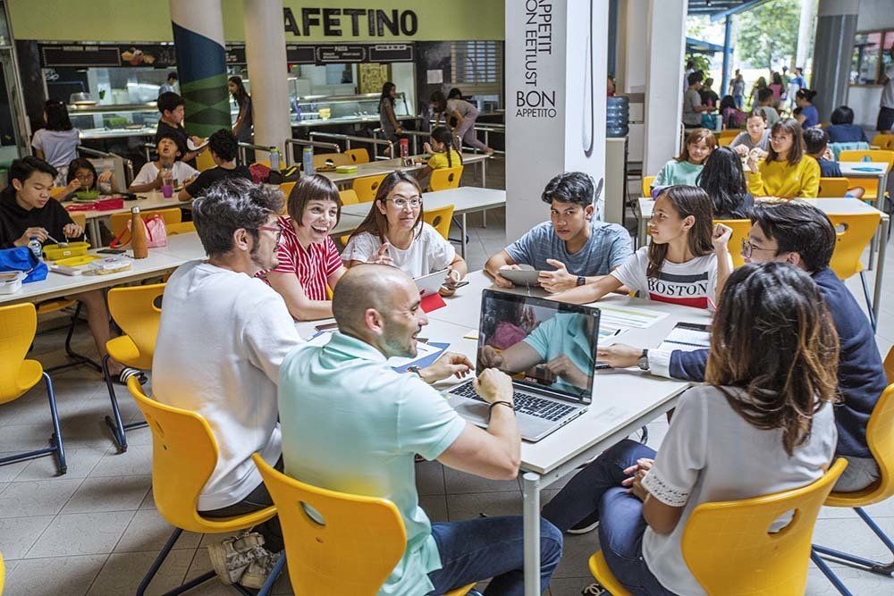 A group of people are sitting around a table with laptops in a cafeteria.