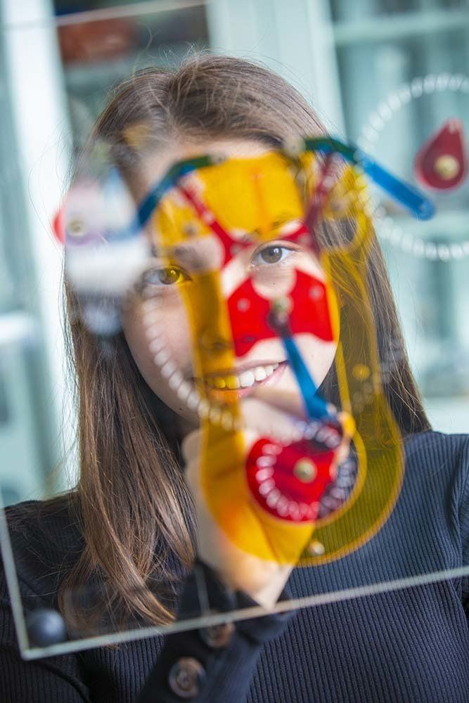 A woman is looking at a colorful clock on a glass wall.