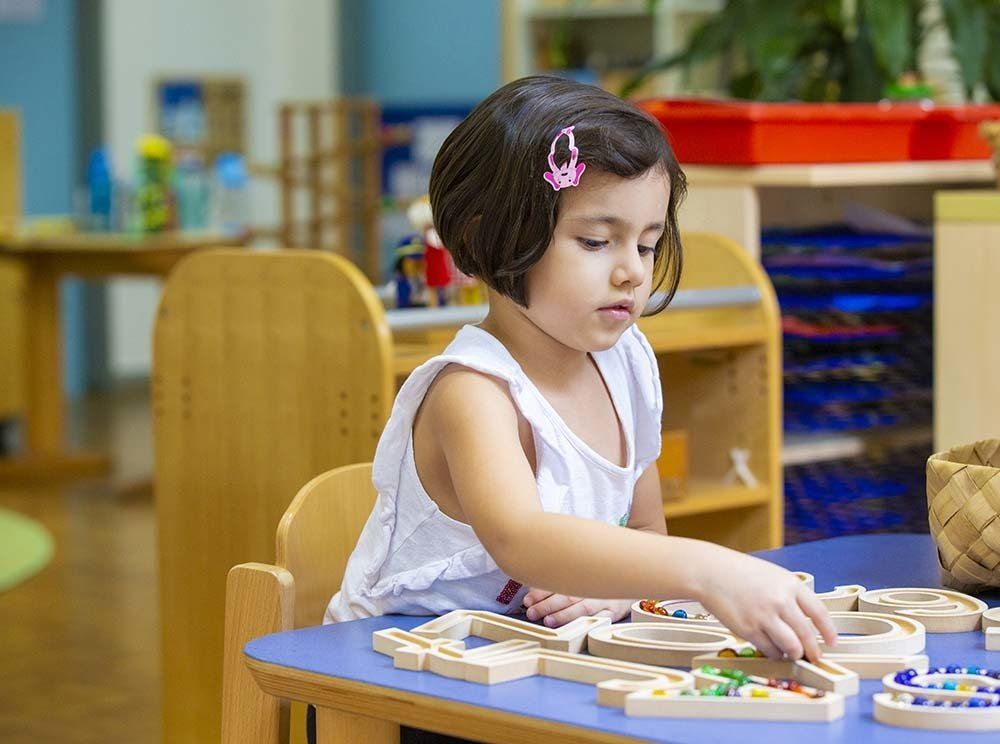 A little girl is sitting at a table playing with wooden toys.