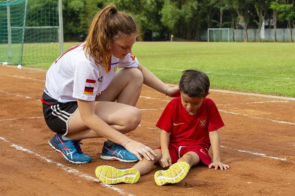 A woman is helping a young boy stretch his legs on a track.