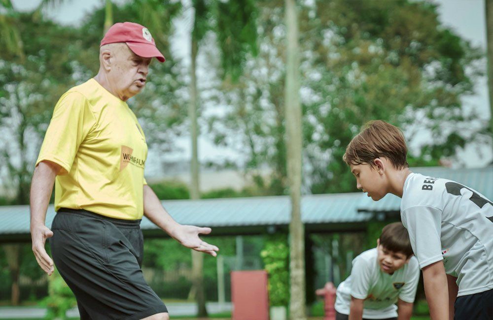 A man in a yellow shirt is talking to two young boys.