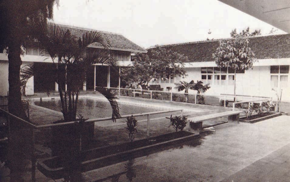 A black and white photo of a swimming pool in front of a building