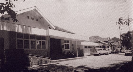 A black and white photo of a building with cars parked in front of it