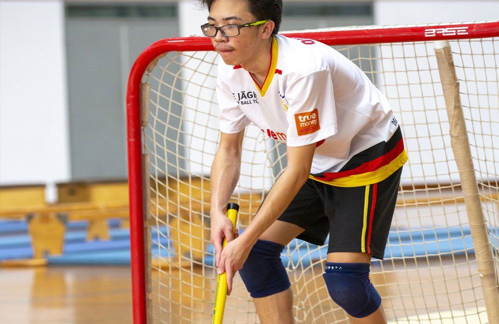 A young man is holding a hockey stick in front of a goal.