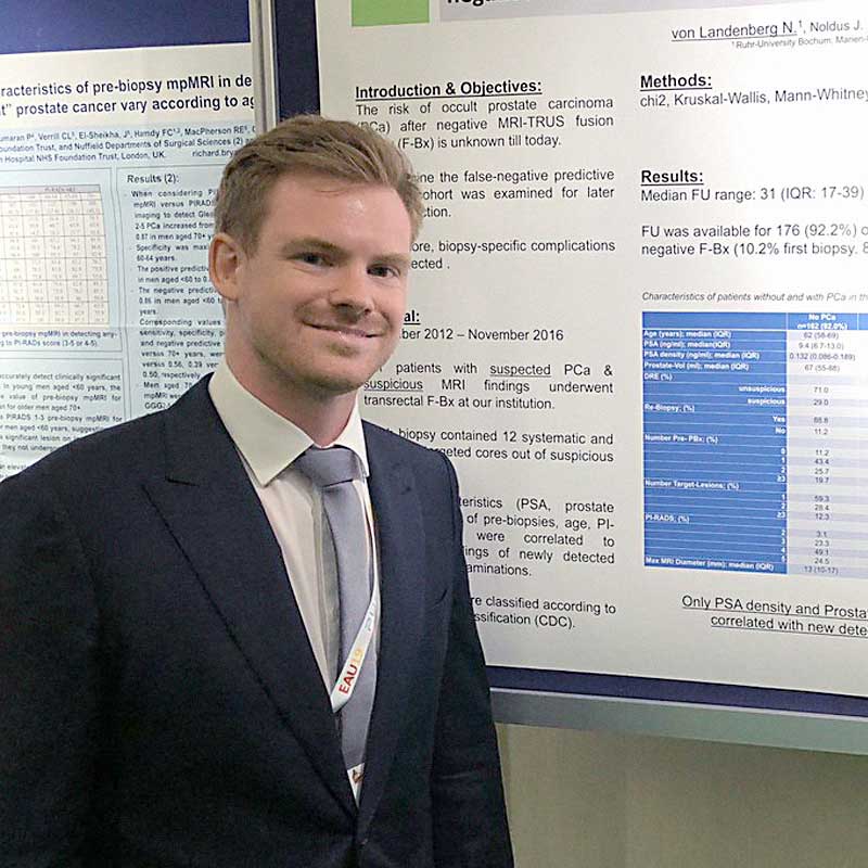 A man in a suit and tie is standing in front of a poster