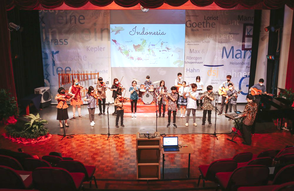 A group of children are playing instruments on a stage in front of a large screen.