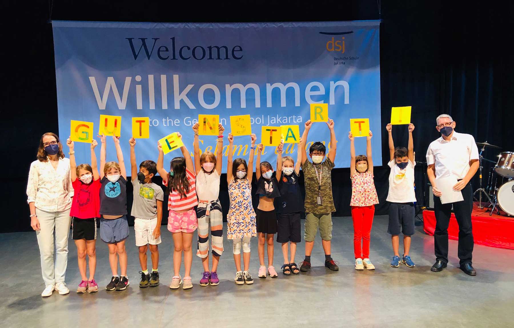 A group of children are standing in front of a sign that says welcome.