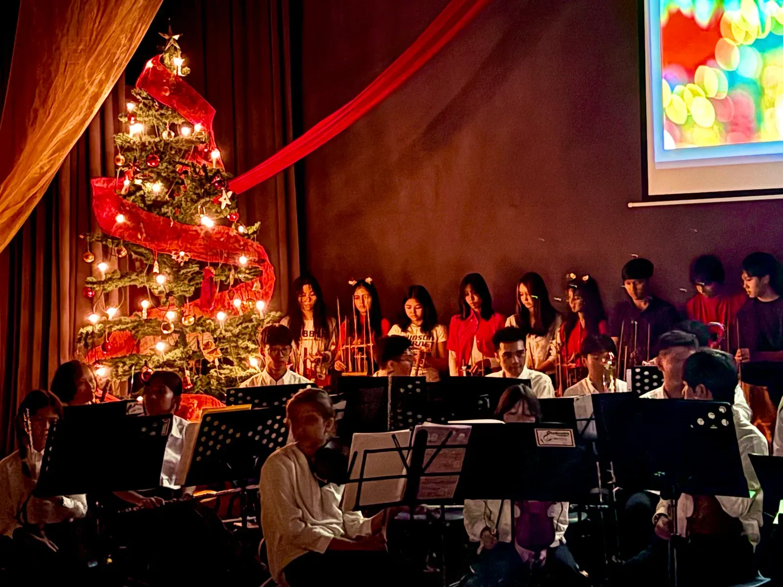 A children orchestra on stage next to a Christmas tree with festive lighting