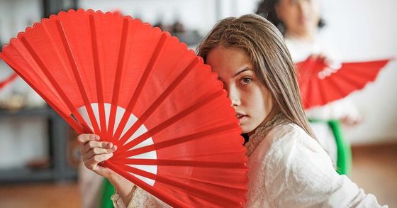 A woman is holding a red fan in front of her face.