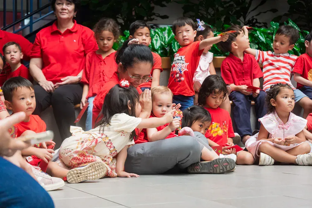 A group of children in red shirts are sitting on the ground.