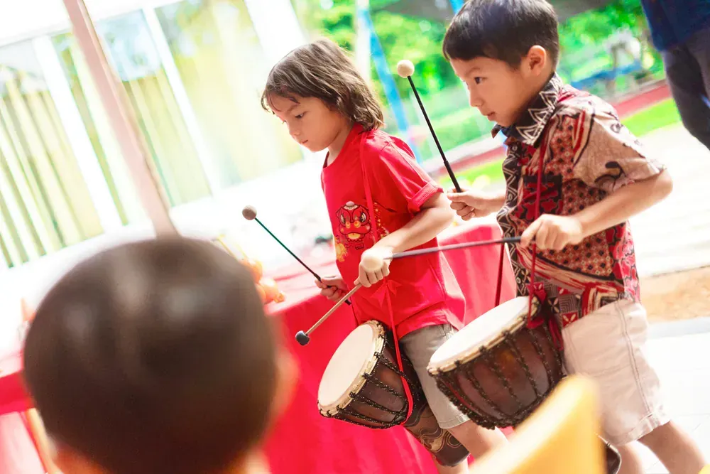 Two young boys are playing drums with sticks in a room.
