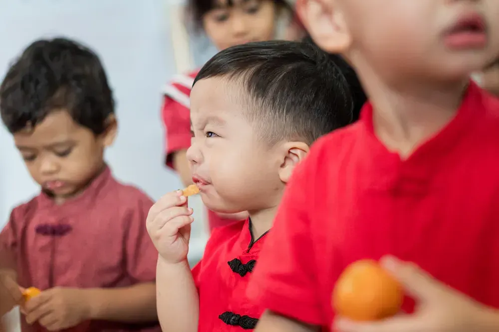 A group of young children are sitting in a row eating food.