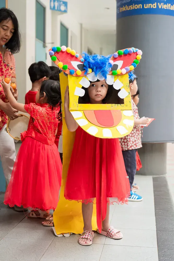 A little girl in a red dress is wearing a dragon costume.