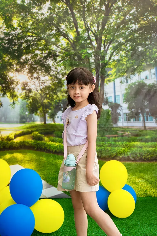 A little girl is standing in front of balloons in a park.