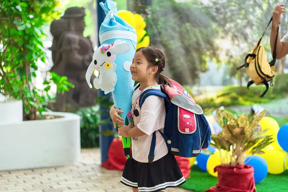 A little girl with a backpack is holding a balloon in the shape of a unicorn.