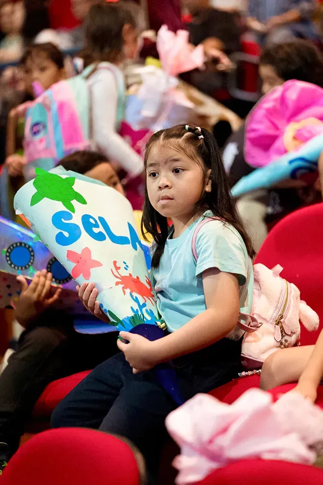 A little girl is sitting in a stadium holding a pillow with the name sel on it.