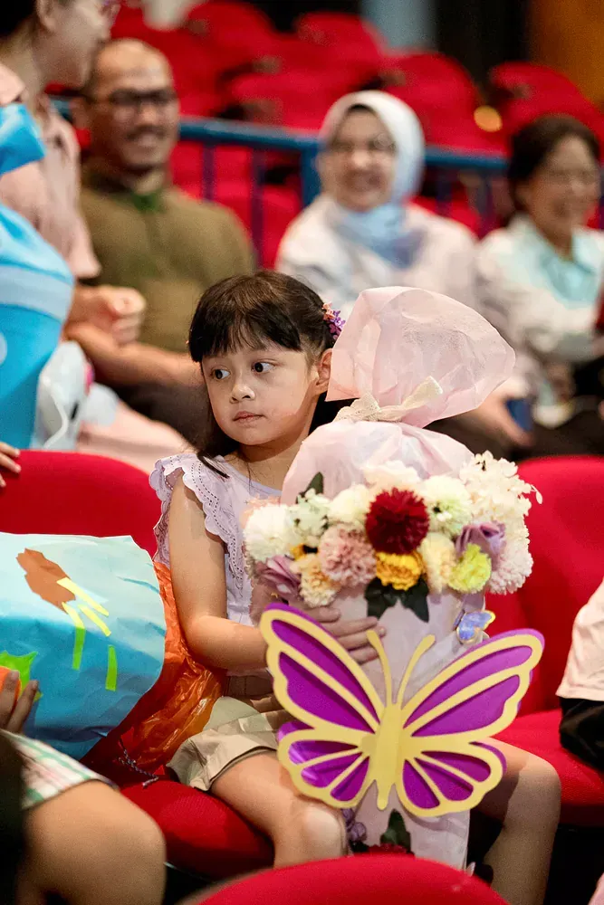 A little girl is sitting in a theatre holding a bouquet of flowers.