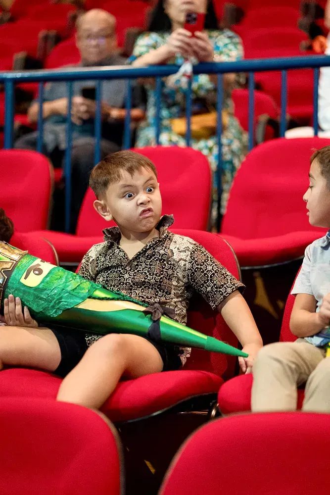 A group of children are sitting in red chairs in a theater.