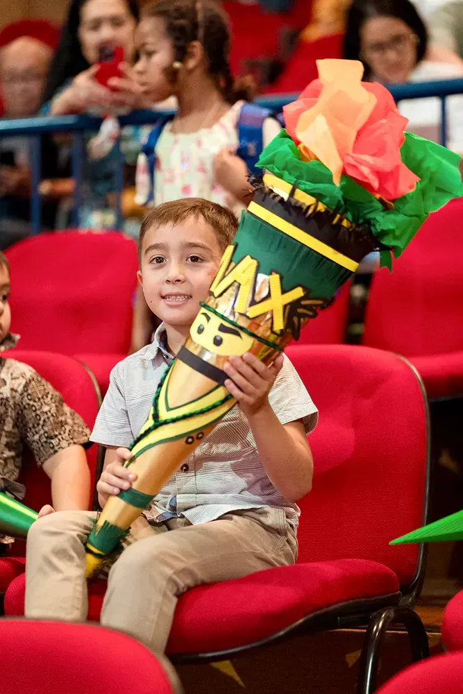 A young boy is sitting in a red chair holding a paper torch.