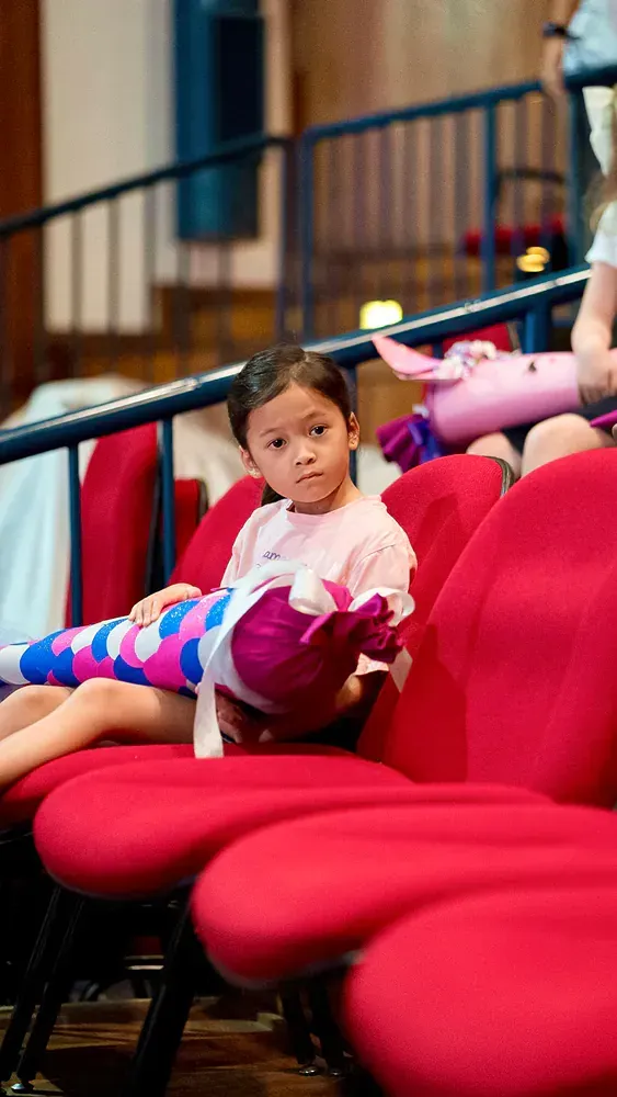 A little girl is sitting in a row of red chairs holding a stuffed animal.