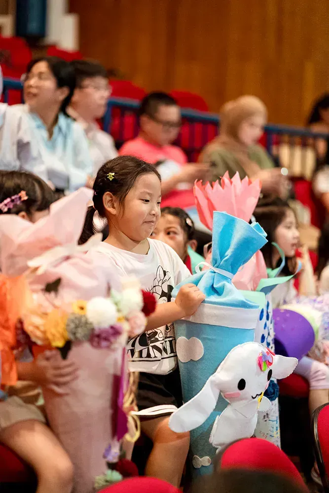 A group of children are sitting in a stadium holding stuffed animals.