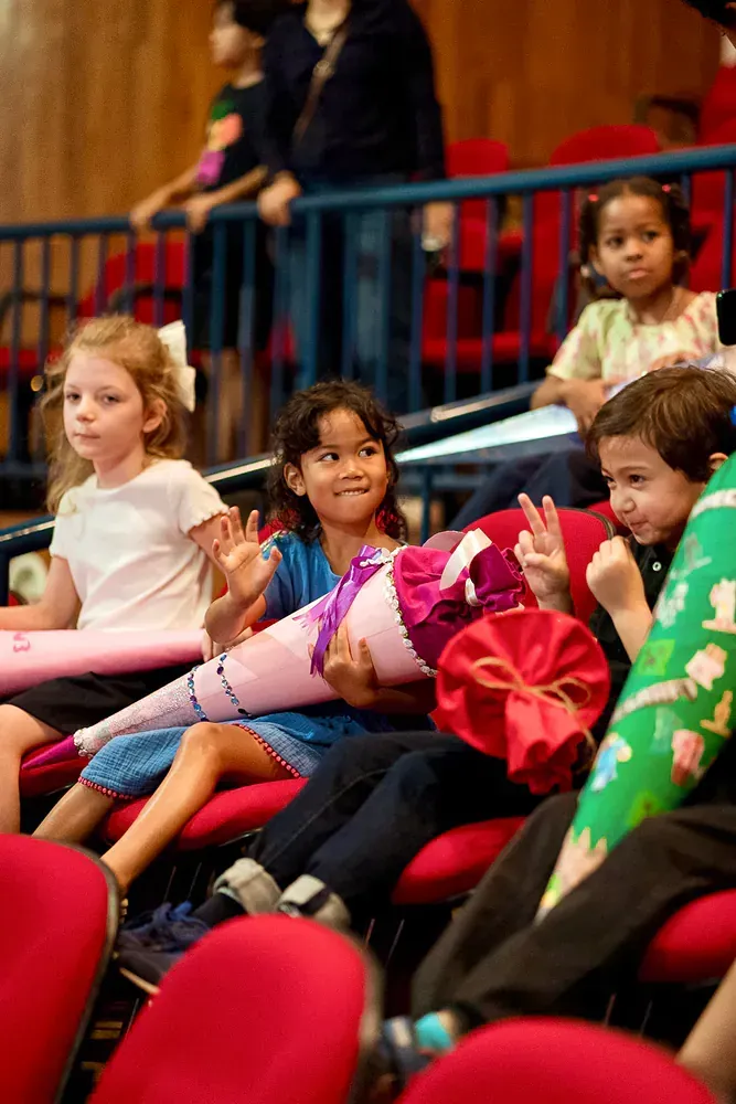 A group of children are sitting in red chairs holding cones.