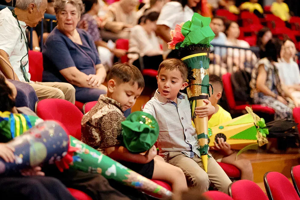A group of children are sitting in a stadium holding cones.