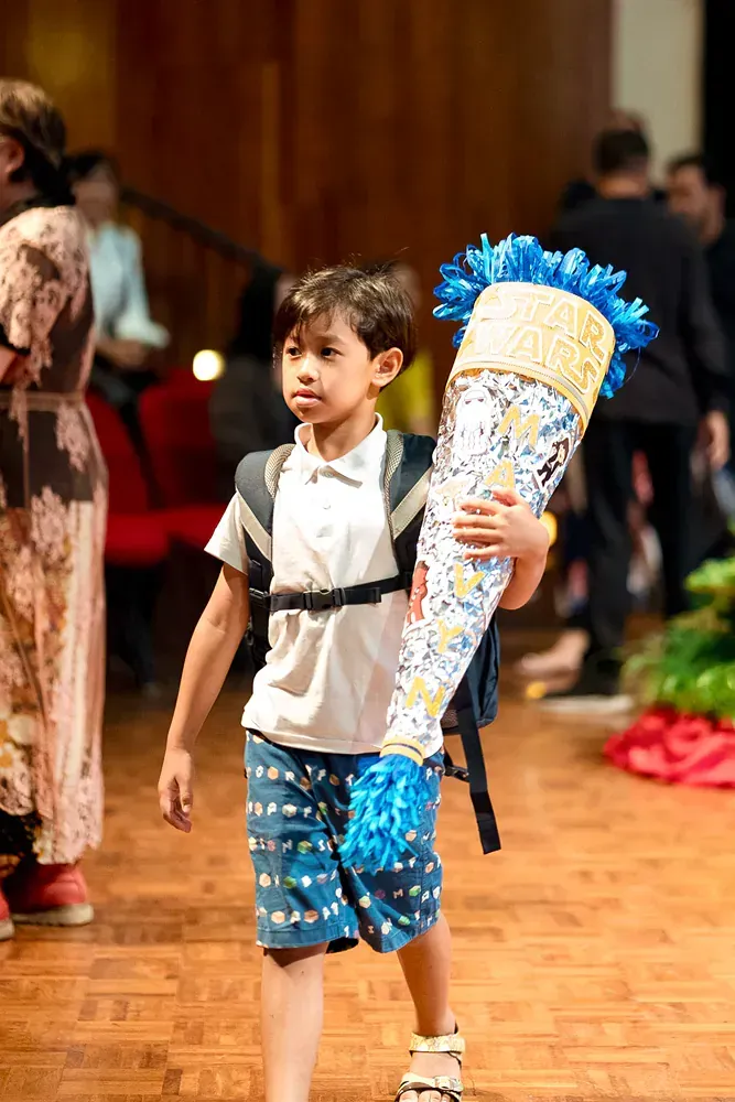 A young boy is carrying a large cone on his back.