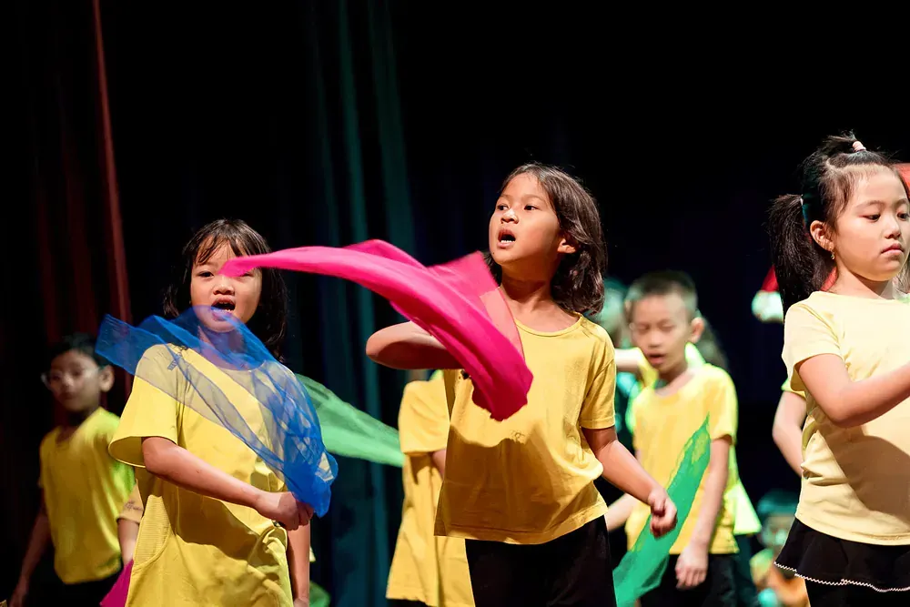 A group of children in yellow shirts are dancing on a stage.