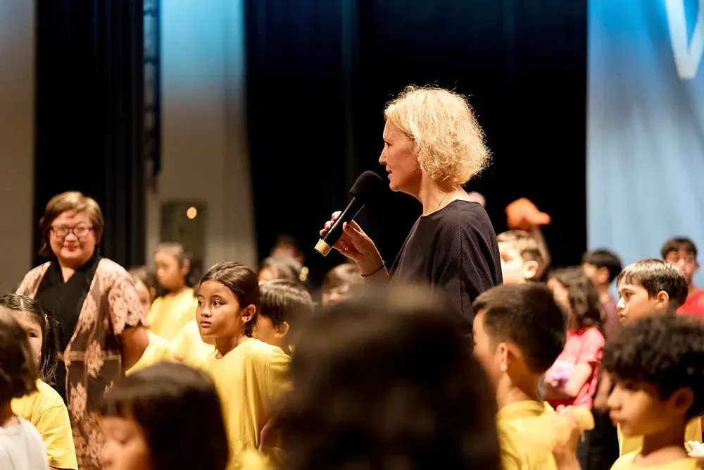 A woman is holding a microphone in front of a crowd of children.