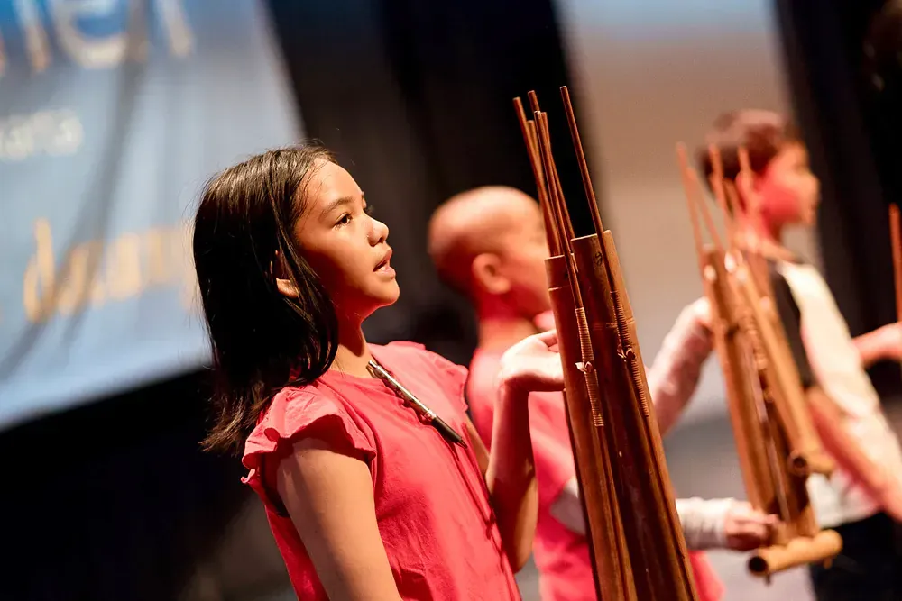 A girl in a red shirt is playing a musical instrument on a stage.