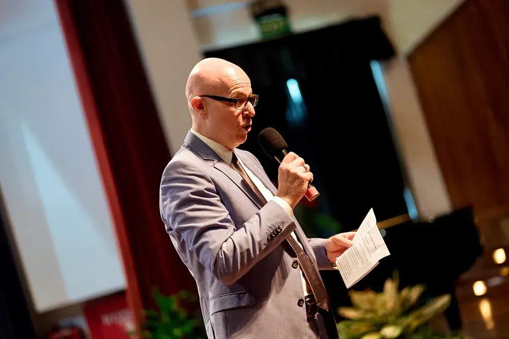 A man in a suit and tie is holding a microphone and giving a speech.