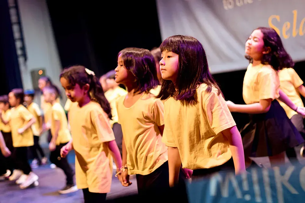 A group of young girls in yellow shirts are dancing on a stage.