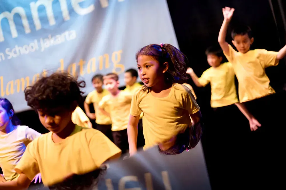 A group of children in yellow shirts are dancing on a stage