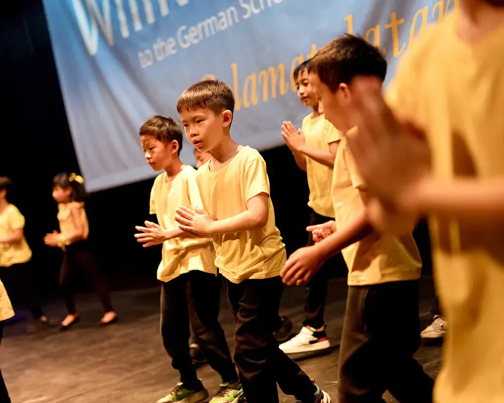 A group of children in yellow shirts are dancing on a stage.