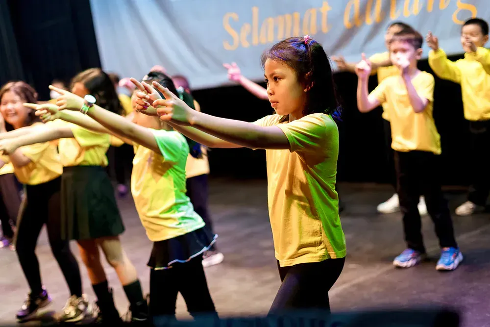 A group of children are dancing in front of a sign that says selamat datang