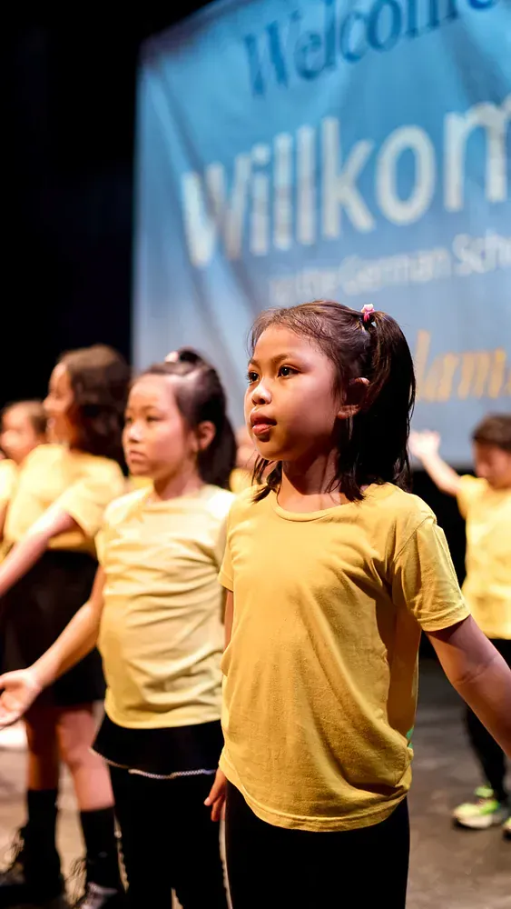 A group of young girls in yellow shirts are dancing on a stage.