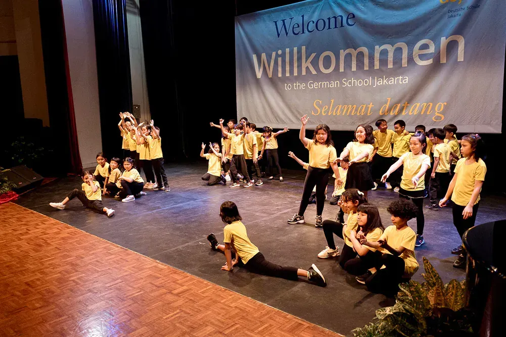 A group of children are dancing on a stage in front of a welcome sign.