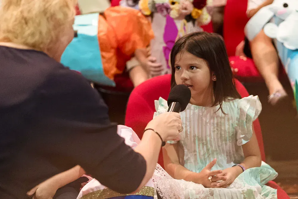 A little girl is sitting in a chair talking into a microphone.