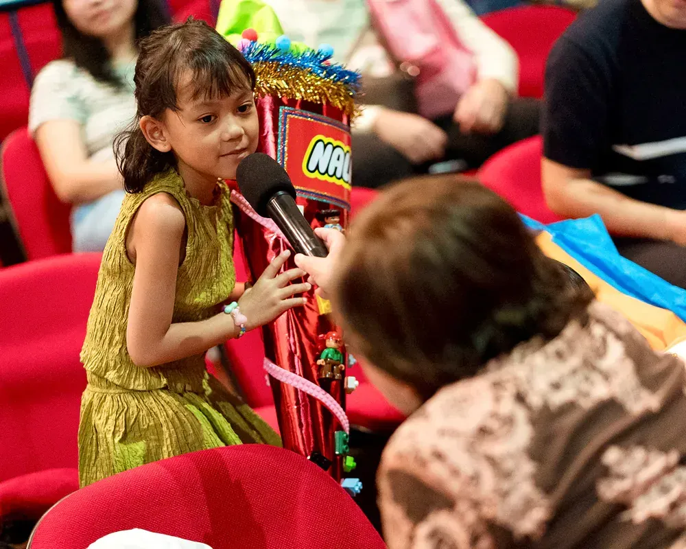A little girl is talking into a microphone in front of a lego box
