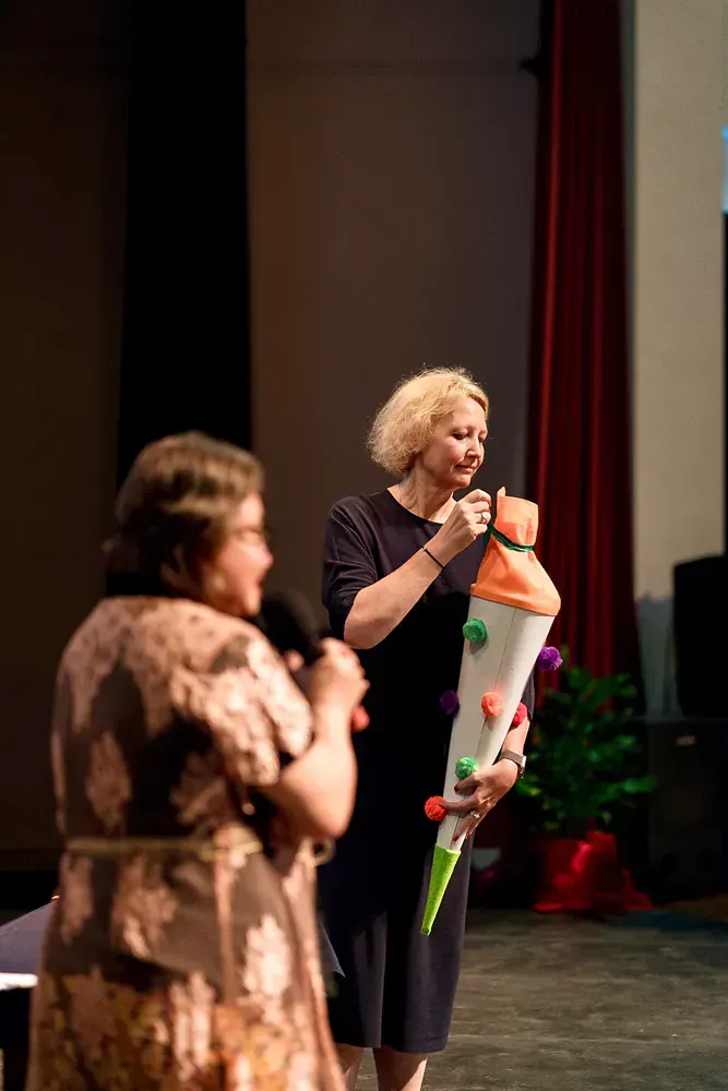 Two women are standing on a stage holding a cone.